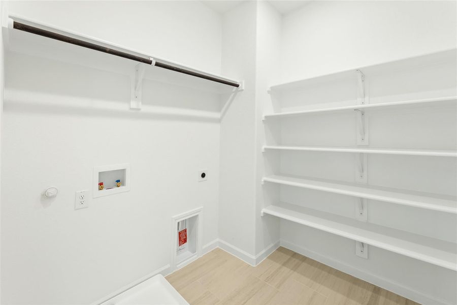 Laundry room with white walls, hanging rod, built-in shelves, and washer hookups on light wood floors