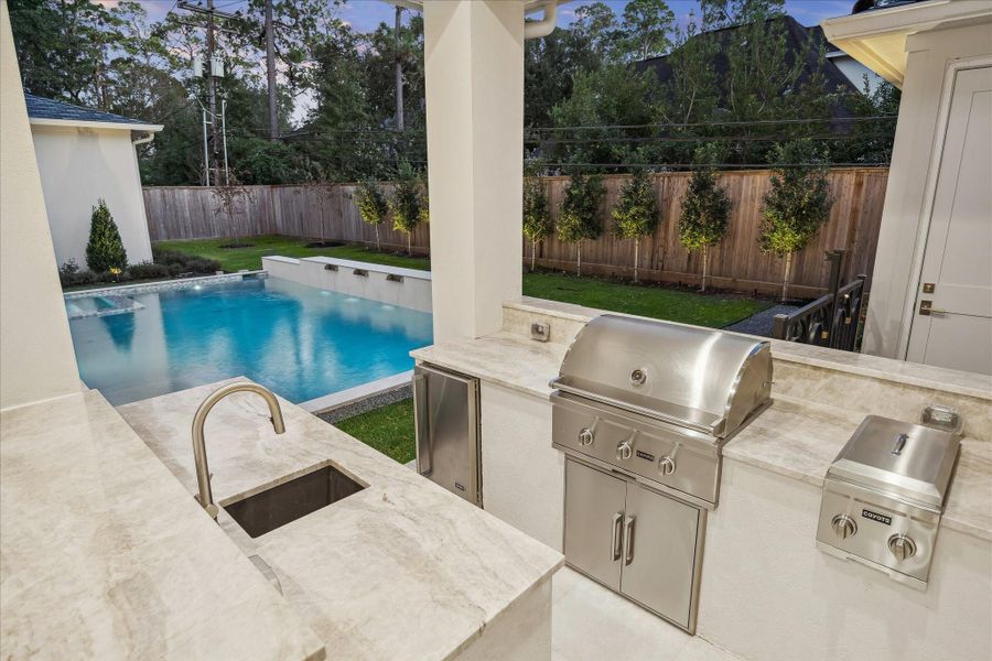 Well appointed al fresco kitchen featuring a built-in grill, side burner, ad under-counter sink set in sleek stone countertops.