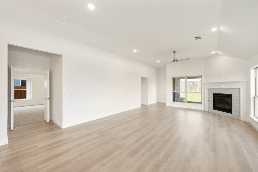 Open living room with light wood floors, fireplace, ceiling fan, and sliding glass door to backyard