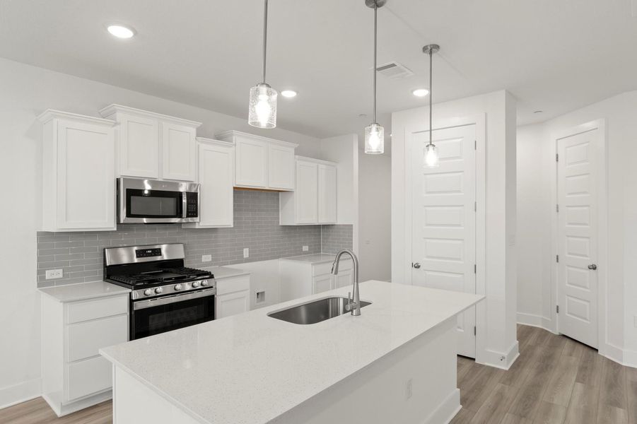 Kitchen with white cabinetry, stainless steel appliances, light stone counters, decorative light fixtures, and backsplash