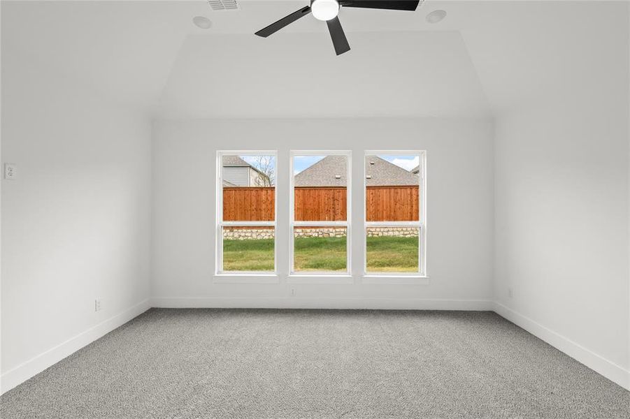 Carpeted empty room with ceiling fan and vaulted ceiling