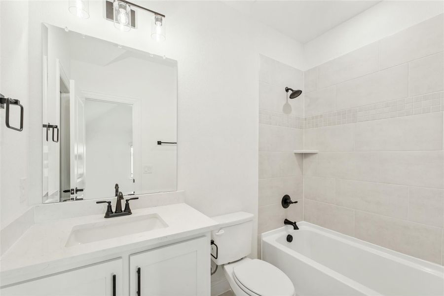 Bathroom with white vanity, single sink, toilet, and tiled shower-tub combo with black fixtures
