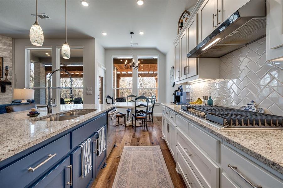 Two tone kitchen with light stone countertops, dark wood-type flooring, stainless steel appliances, two tone color scheme, and suspended lighting