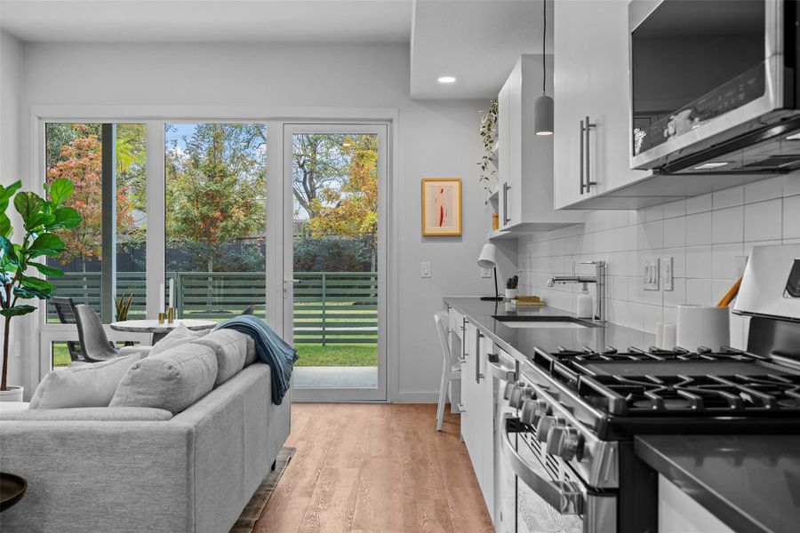 Kitchen with a sink, appliances with stainless steel finishes, decorative backsplash, light wood finished floors, and dark countertops