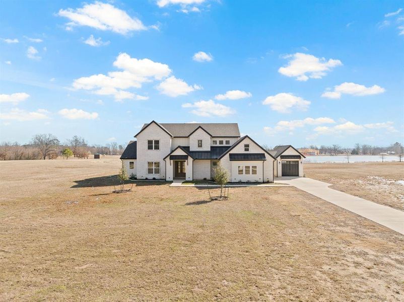 View of front of property with concrete driveway, a garage, a front yard, a standing seam roof, and metal roof View of front of property with concrete driveway, a garage, a front yard, a standing seam roof, and metal roof