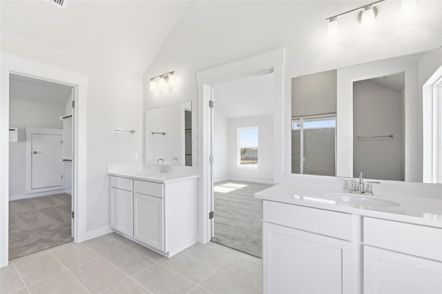 Bathroom with light carpet, vaulted ceiling, light tile patterned floors, two vanities, and track lighting