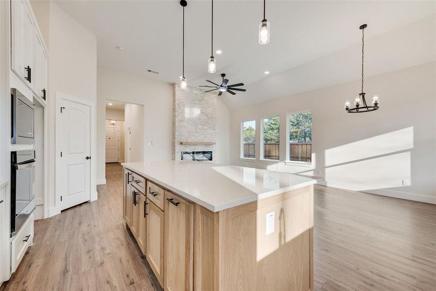 Kitchen featuring open floor plan, light brown cabinets, a center island, pendant lighting, and lofted ceiling