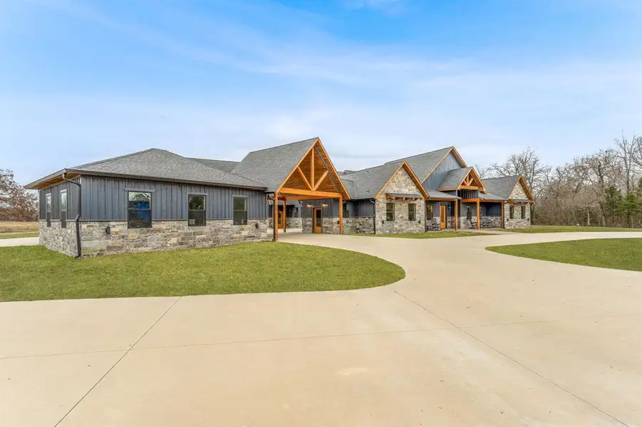 Modern farmhouse style home featuring stone siding, board and batten siding, a front lawn, and curved driveway
