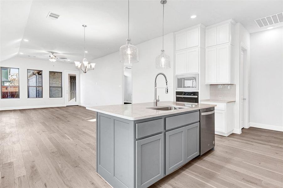 Kitchen with ceiling fan with notable chandelier, sink, hanging light fixtures, an island with sink, and tasteful backsplash