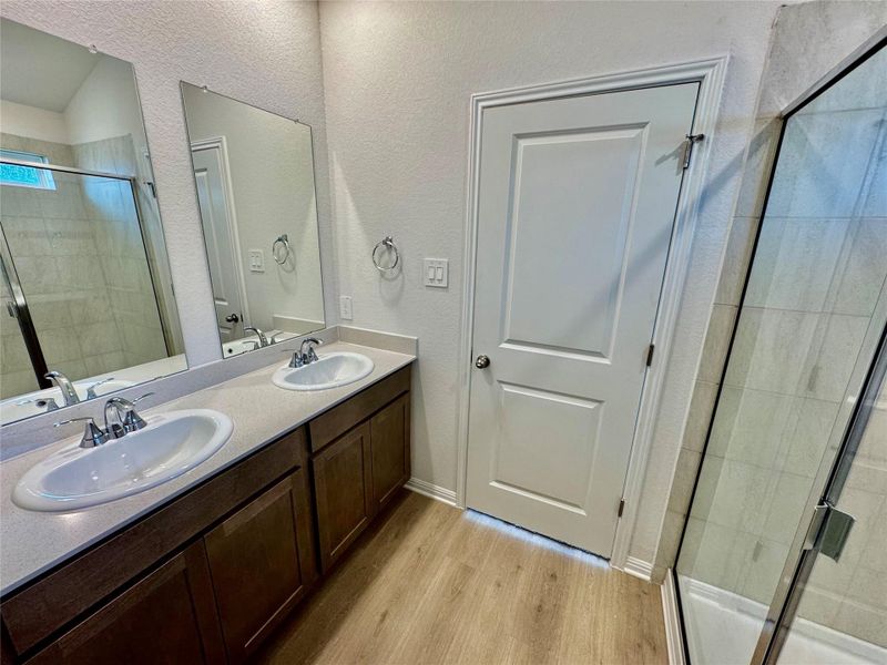 Full bathroom featuring light wood-style flooring, a shower stall, double vanity, and a textured wall