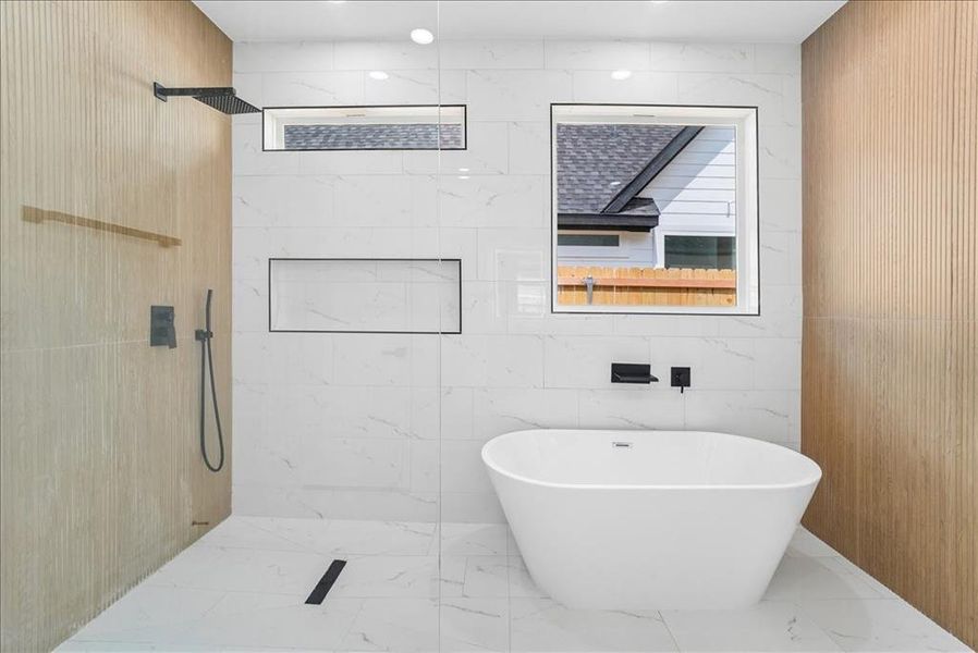 Contemporary bathroom featuring a freestanding soaking tub, large format white tile walls and flooring, and a walk-in shower with a rainfall showerhead Contemporary bathroom featuring a freestanding soaking tub, large format white tile walls and flooring, and a walk-in shower with a rainfall showerhead