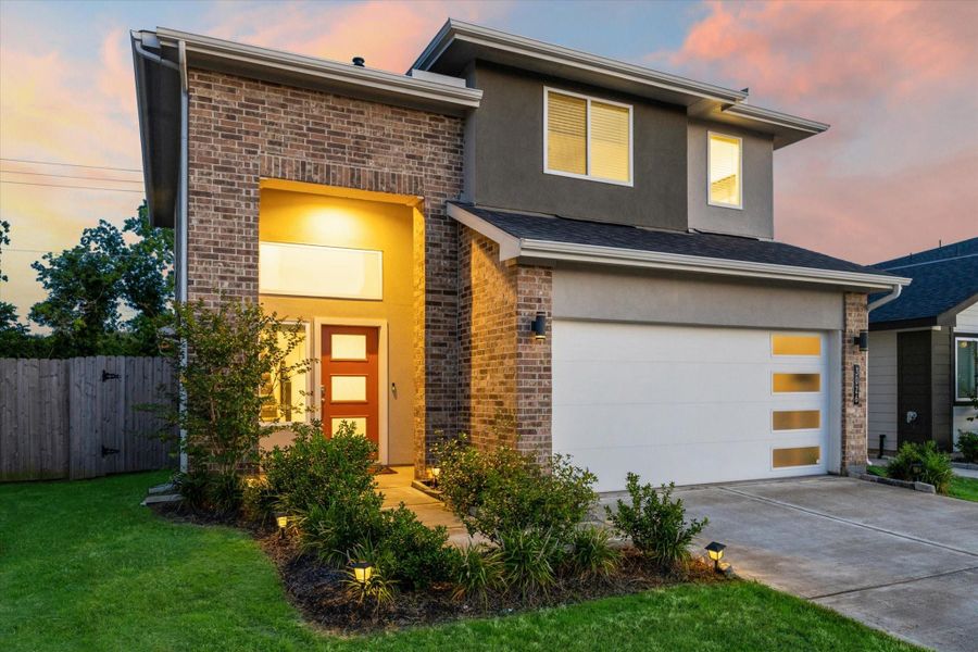 Modern curb appeal meets warm welcome in this two-story brick home with bold architectural lines, up-lighted landscaping, and a sleek glass-paneled garage door. Evening illumination highlights the striking entry and designer front door, setting the tone for the stylish interior that follows. Modern curb appeal meets warm welcome in this two-story brick home with bold architectural lines, up-lighted landscaping, and a sleek glass-paneled garage door. Evening illumination highlights the striking entry and designer front door, setting the tone for the stylish interior that follows.