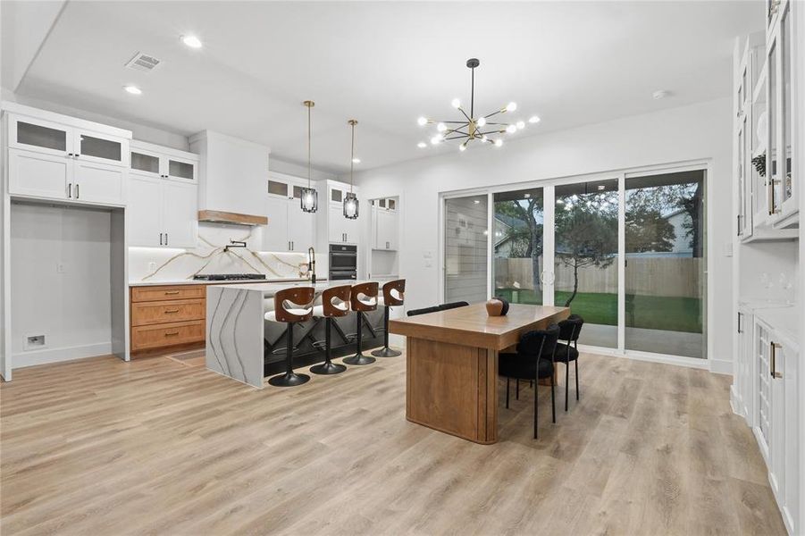 Kitchen featuring glass fronted cabinets, an island with sink, a kitchen breakfast bar, light wood-style flooring, and a chandelier