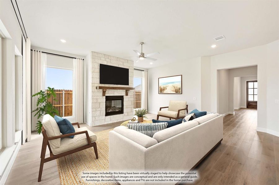 Living room with stone fireplace, hardwood floors, ceiling fan, and large windows letting in natural light