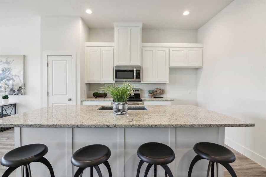 Kitchen featuring a breakfast bar area, white cabinetry, an island with sink, and light stone counters