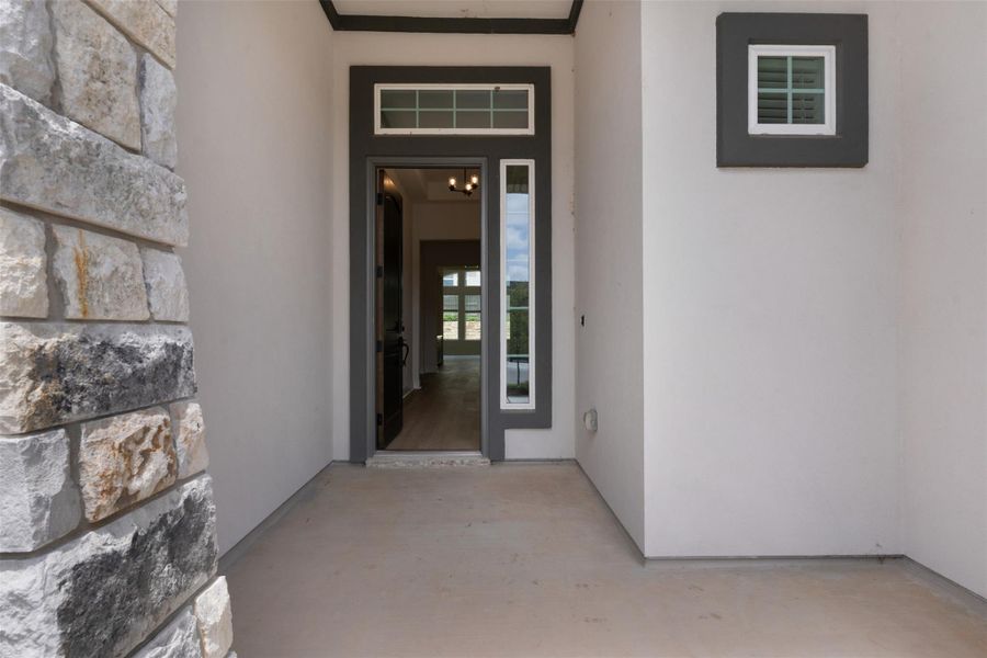 Entryway featuring a stone column, a dark-framed door with sidelights and transom, and a square window with white trim Entryway featuring a stone column, a dark-framed door with sidelights and transom, and a square window with white trim