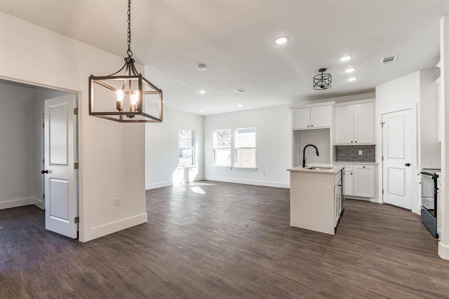 Kitchen featuring range with electric cooktop, decorative light fixtures, an island with sink, sink, and white cabinets