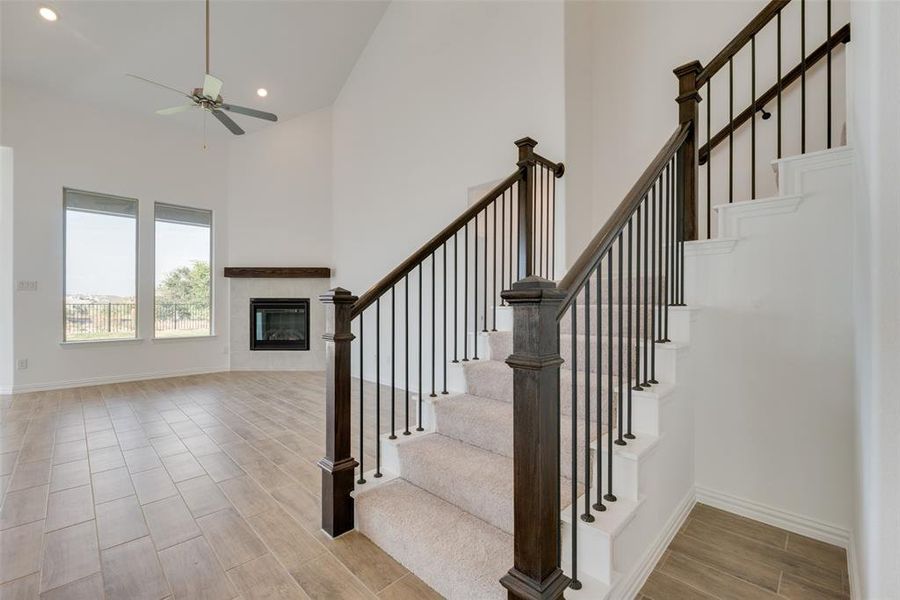 Stairs with a tile fireplace, ceiling fan, hardwood / wood-style floors, and a towering ceiling