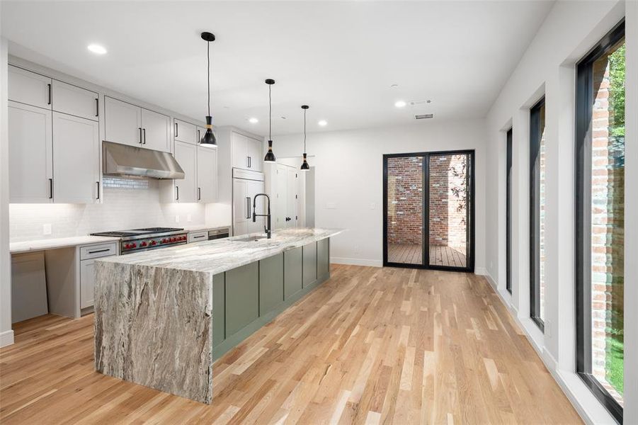 Kitchen featuring light stone countertops, stovetop, a kitchen island with sink, and sink