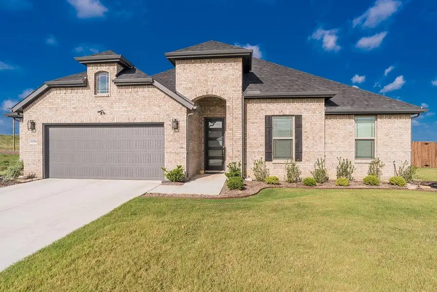Brick exterior residence with a dark shingle roof, arched entry with a modern door, and a 2.5-car garage