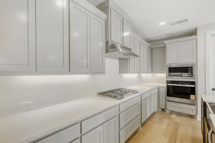 Kitchen with stainless steel appliances, light wood-style flooring, tasteful backsplash, recessed lighting, and beverage cooler