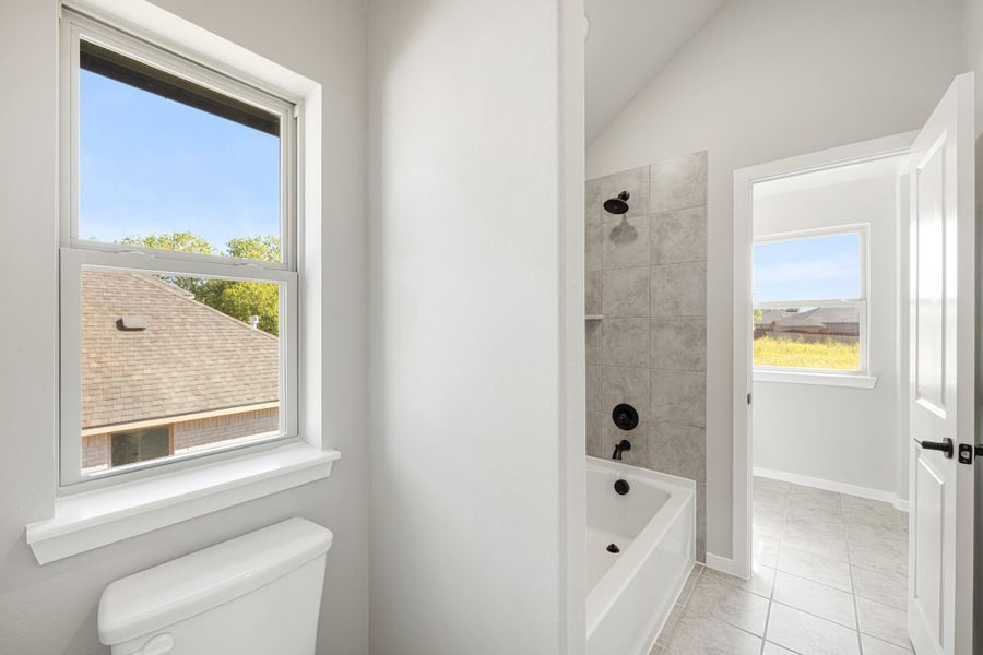 Bathroom with soaking tub, gray tile shower surround, black fixtures, toilet, and large window with natural light.