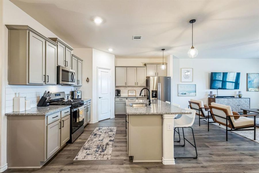 Kitchen featuring light stone countertops, stainless steel appliances, tasteful backsplash, sink, and hanging light fixtures