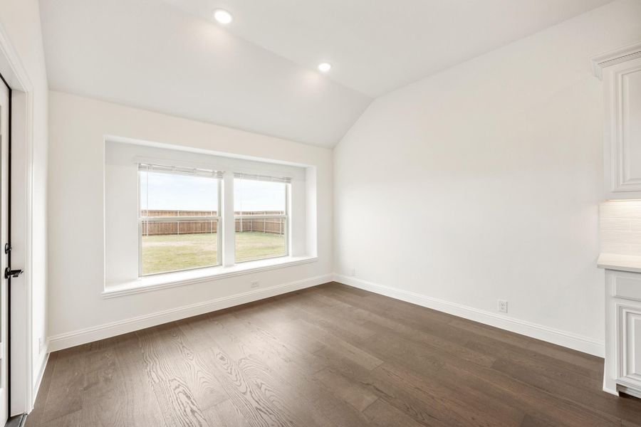 Empty room with vaulted ceiling, dark hardwood floors, and large window overlooking fenced backyard