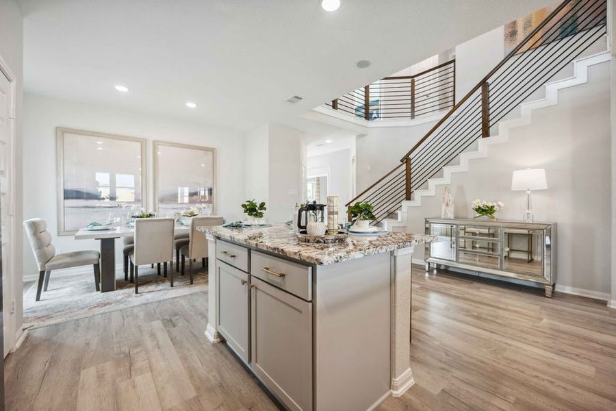 Open-concept dining area with kitchen island, granite countertops, and modern staircase with cable railing