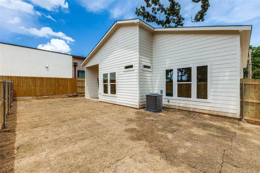 Expansive backyard featuring a newly installed wooden fence, white horizontal siding, a central air conditioning unit, and multiple large windows Expansive backyard featuring a newly installed wooden fence, white horizontal siding, a central air conditioning unit, and multiple large windows