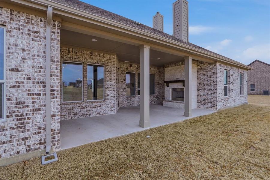 Back of property featuring a fireplace, a patio area, brick siding, and a lawn