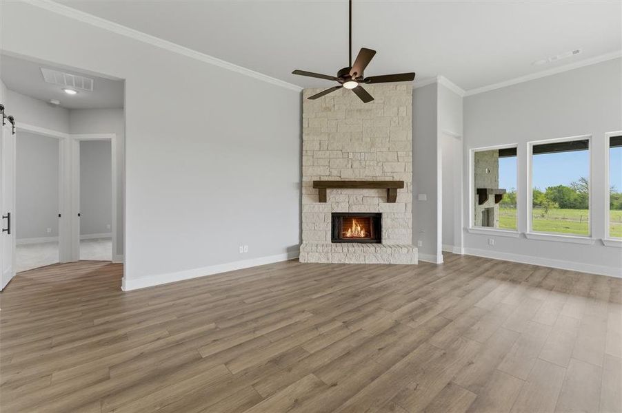 Unfurnished living room featuring light wood-style flooring, ornamental molding, ceiling fan, and a fireplace