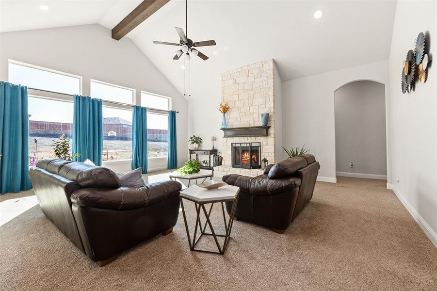 Carpeted living room featuring ceiling fan, high vaulted ceiling, beam ceiling, and a fireplace Carpeted living room featuring ceiling fan, high vaulted ceiling, beam ceiling, and a fireplace