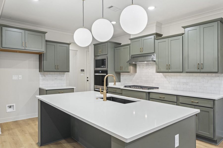 Modern kitchen featuring a large central island with a white countertop, sage green cabinetry, a gas cooktop, and built-in wall oven and microwave Modern kitchen featuring a large central island with a white countertop, sage green cabinetry, a gas cooktop, and built-in wall oven and microwave