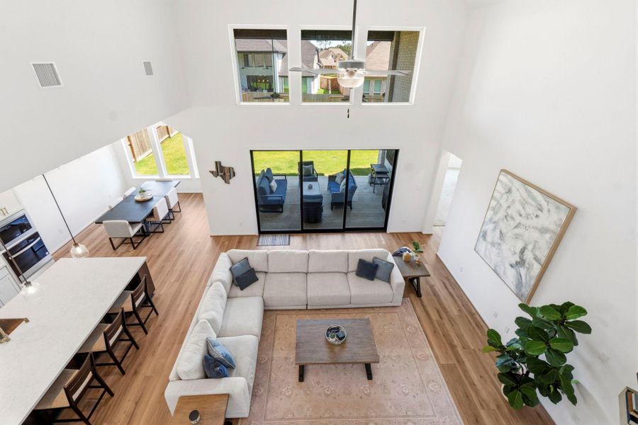 This bright and spacious open-concept living area features high ceilings, large windows, double sliding glass doors lead to an outdoor patio, perfect for entertaining. and elegant wood look vinyl floors. It includes a modern kitchen with a large island, a cozy living room and a dining area with ample natural light.