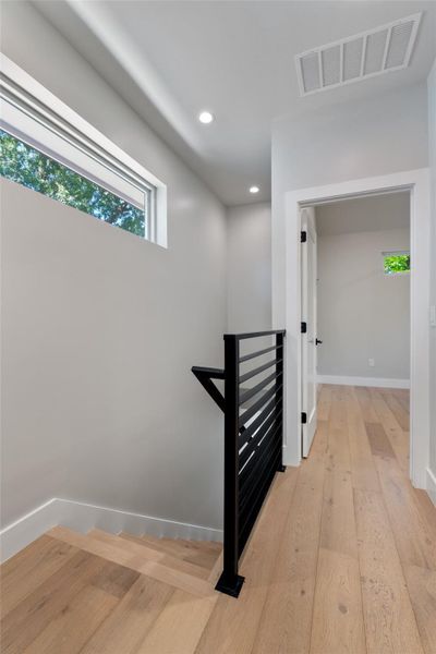 Upstairs. Modern interior featuring light wood-finish flooring, recessed lighting, and a contemporary black metal stair railing Upstairs. Modern interior featuring light wood-finish flooring, recessed lighting, and a contemporary black metal stair railing