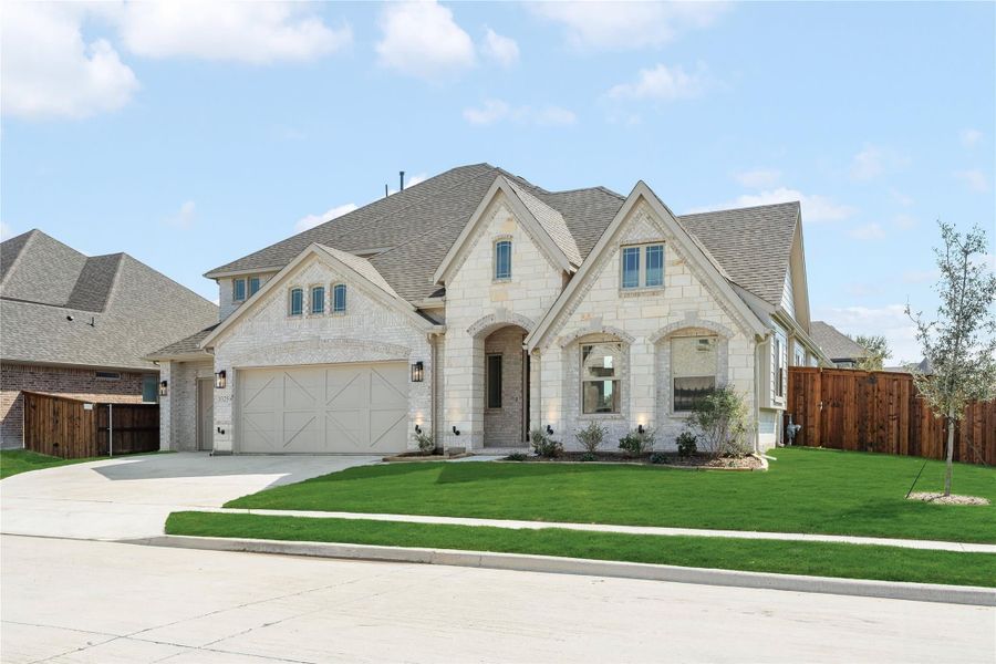 Single-story home with light stone exterior, two-car garage, arched entry, and manicured front lawn