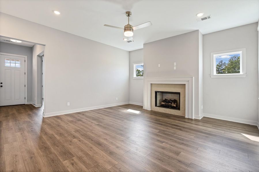 Recessed lighting, wood-finish flooring, a ceiling fan, a fireplace with a white surround, and an entry door with glass inserts