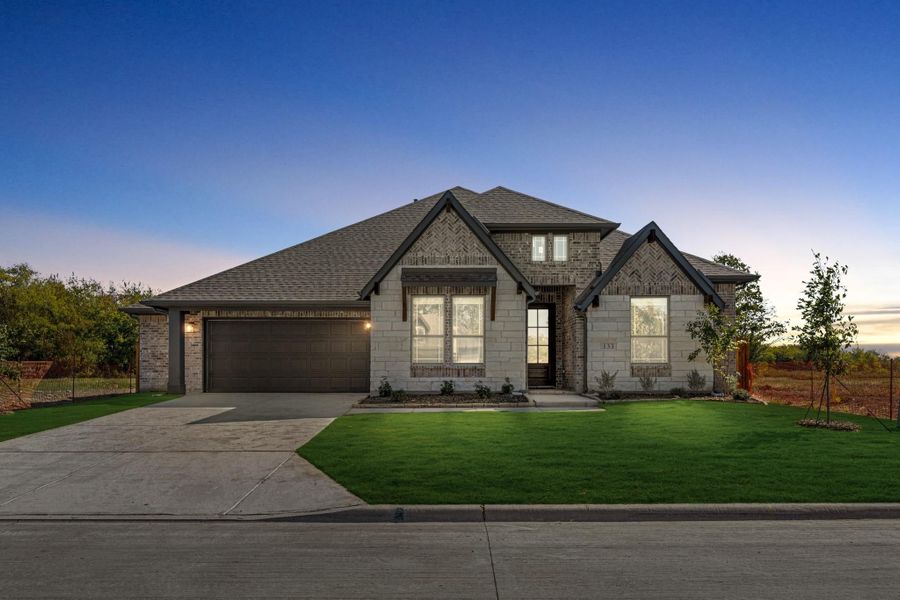 Single-story home with brick and stone exterior, two-car garage, and green front lawn at dusk Single-story home with brick and stone exterior, two-car garage, and green front lawn at dusk
