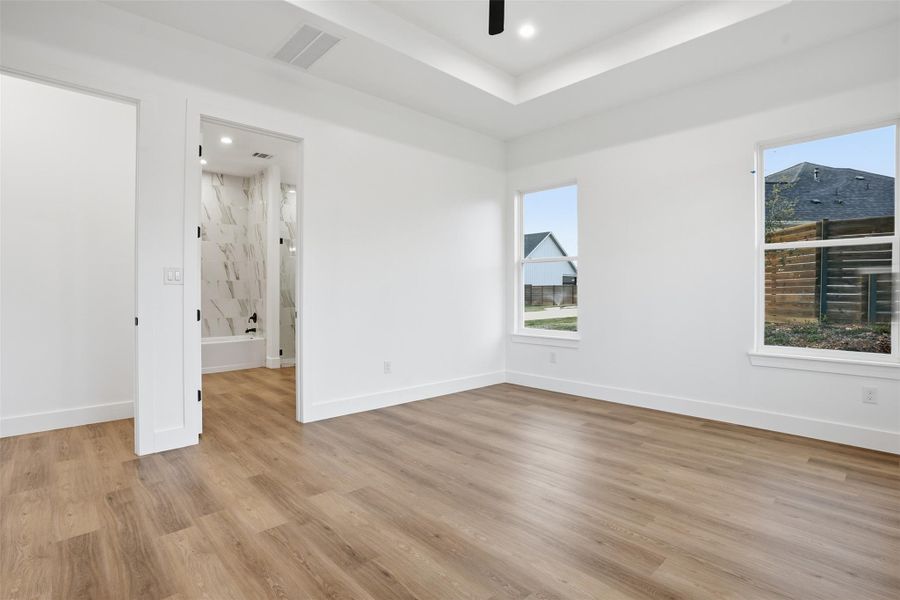 Unfurnished bedroom featuring recessed lighting, a ceiling fan, light wood-style flooring, connected bathroom, and a tray ceiling