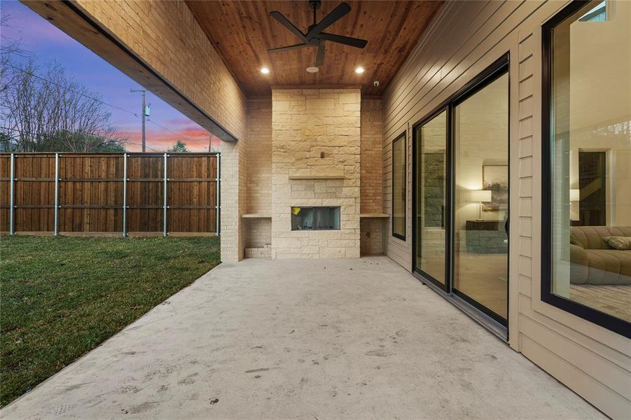 Patio terrace at dusk with an outdoor stone fireplace, a ceiling fan, and a patio area