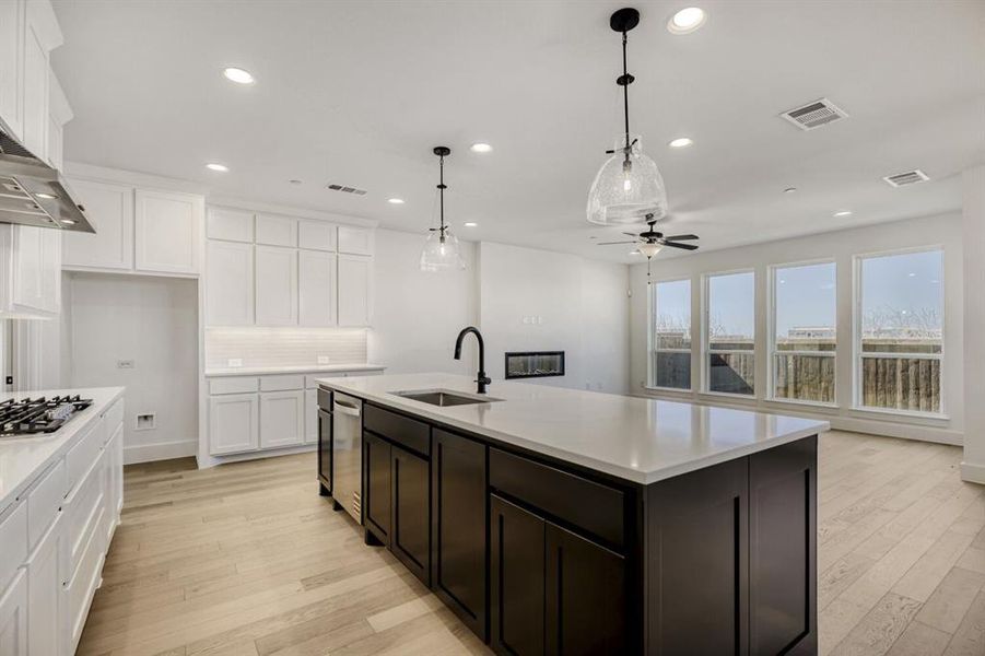 Dual tone kitchen with hanging light fixtures, a ceiling fan, light wood-type flooring, an island with sink, and two tone color scheme