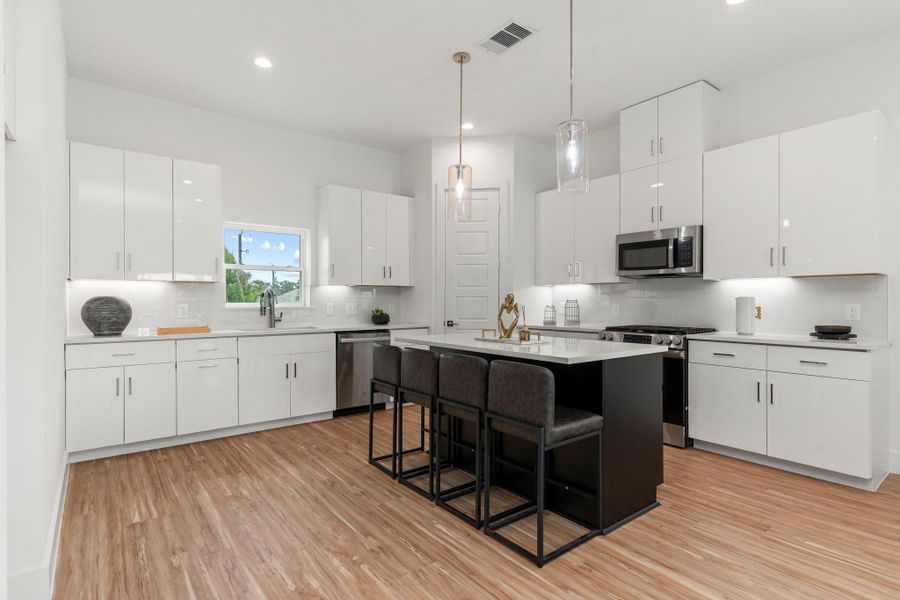 Abundant counter space and cabinetry meet modern style in this open-concept kitchen, featuring a central island with pendant lighting and room for casual seating—seamlessly connected to the living area for effortless entertaining