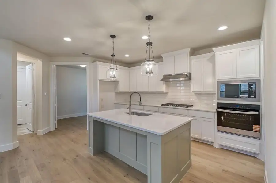 Kitchen featuring stainless steel appliances, a center island with sink, light wood finished floors, decorative light fixtures, and backsplash Kitchen featuring stainless steel appliances, a center island with sink, light wood finished floors, decorative light fixtures, and backsplash