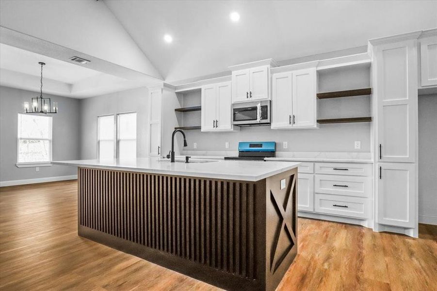 Kitchen with a kitchen island with sink, black stove, and white cabinets