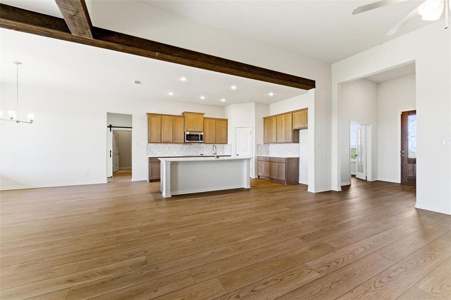 Unfurnished living room featuring a barn door, beamed ceiling, light wood-style flooring, ceiling fan, and a chandelier