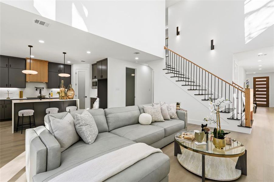 Living area with stairs, light wood finished floors, a high ceiling, and recessed lighting