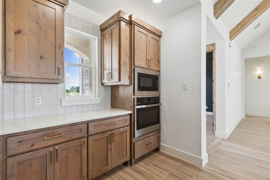 Kitchen featuring stainless steel oven, vaulted ceiling with beams, decorative backsplash, light wood-type flooring, and black microwave