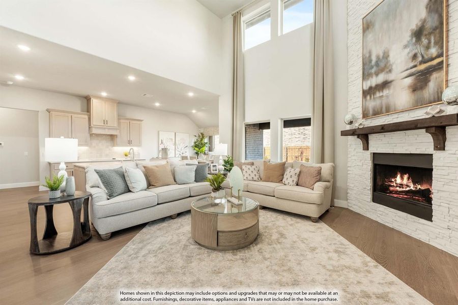Open living room with two-story ceiling, stone fireplace, and open kitchen in background