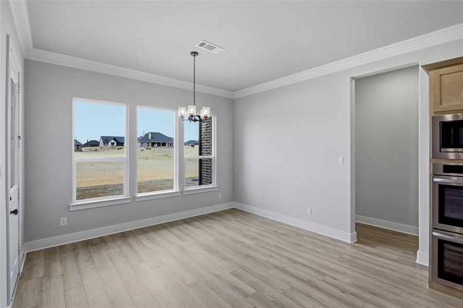 Unfurnished dining area with suspended lighting, ornamental molding, light wood-style flooring, and a residential view